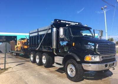 A large black dump truck parked on a sunny day near a building with blue accents.
