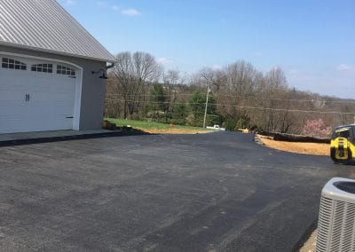 Freshly paved driveway beside a house with a garage, under a clear blue sky.