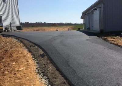 A freshly paved asphalt driveway leading to a garage, with a clear sky above and bare ground on the sides.