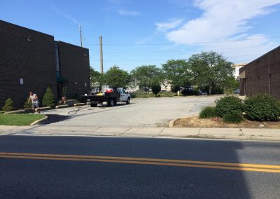 A truck parked in a lot between two brick buildings, with a person walking on the sidewalk nearby.