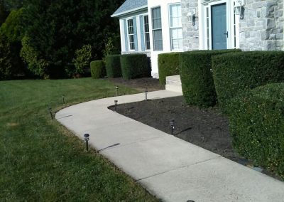 Front of a house with a stone facade, a curved sidewalk, well-trimmed hedges, and grassy lawn.
