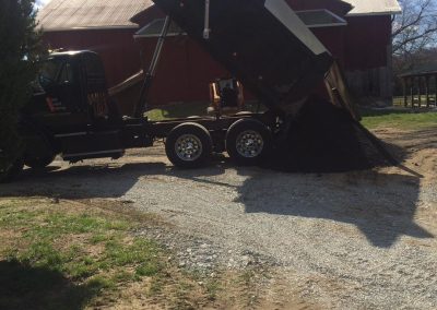 Dump truck tipping gravel near red barn