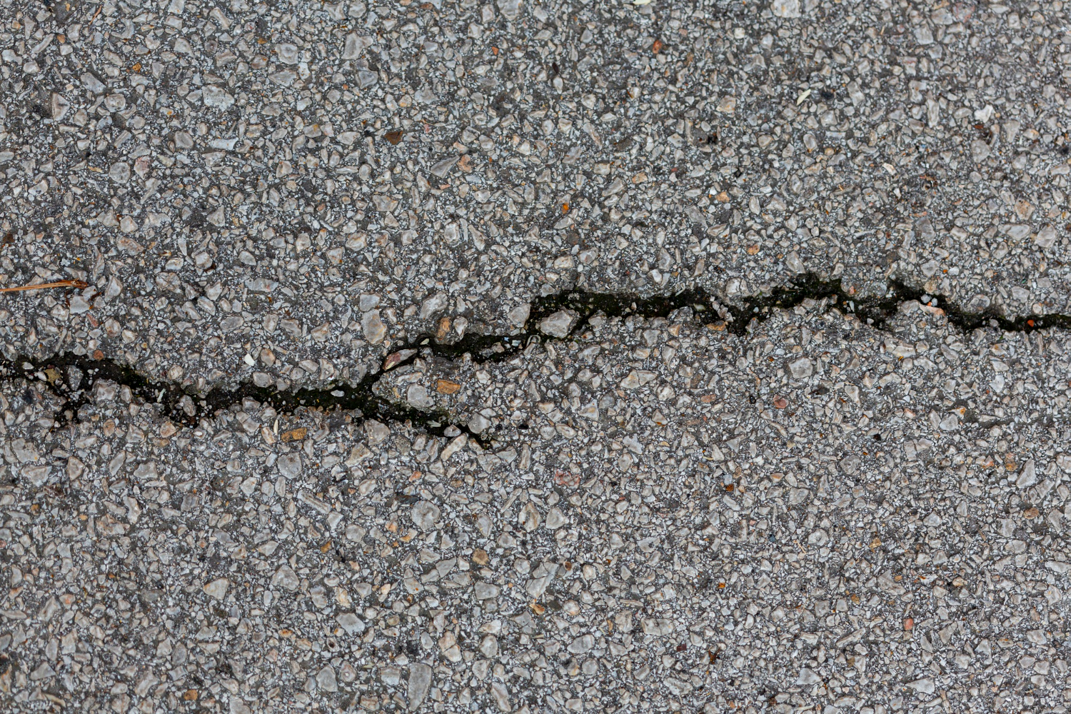 2148394711 Cracked asphalt surface with a jagged line running through the gray, textured gravel surface.
